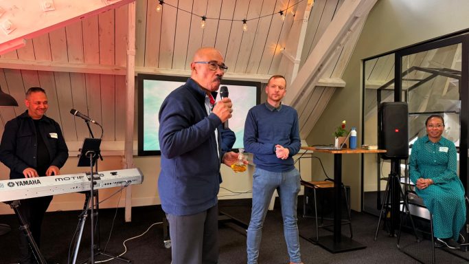 Twee sprekers op een evenement met muziekachtergrond en een publiek.